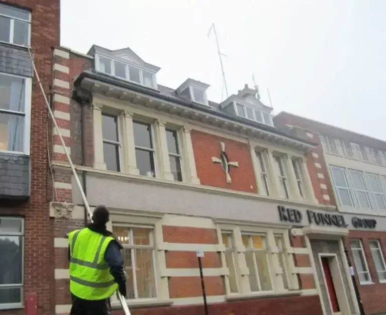 Commercial window cleaner in a high-visibility vest using an extended pole system to clean upper-floor windows on the Red Funnel Group building, demonstrating Neptune Window Cleaning’s commercial services.
