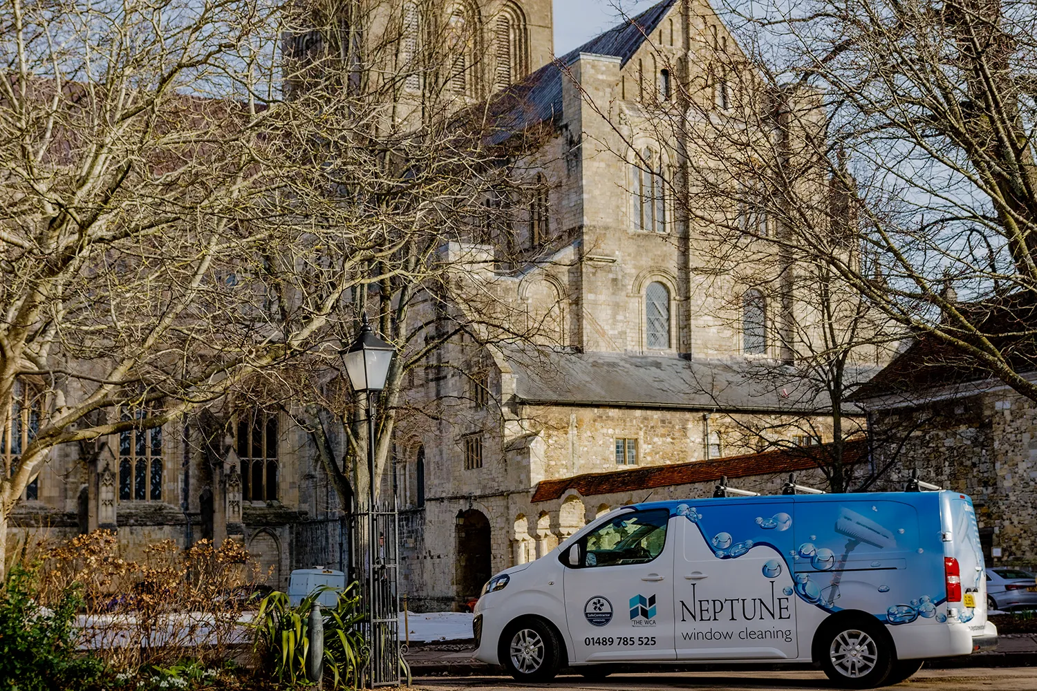 A Neptune Window Cleaning van parked outside a historic stone church, showing the company’s blue and white branding, representing professional window cleaning services in a heritage setting.